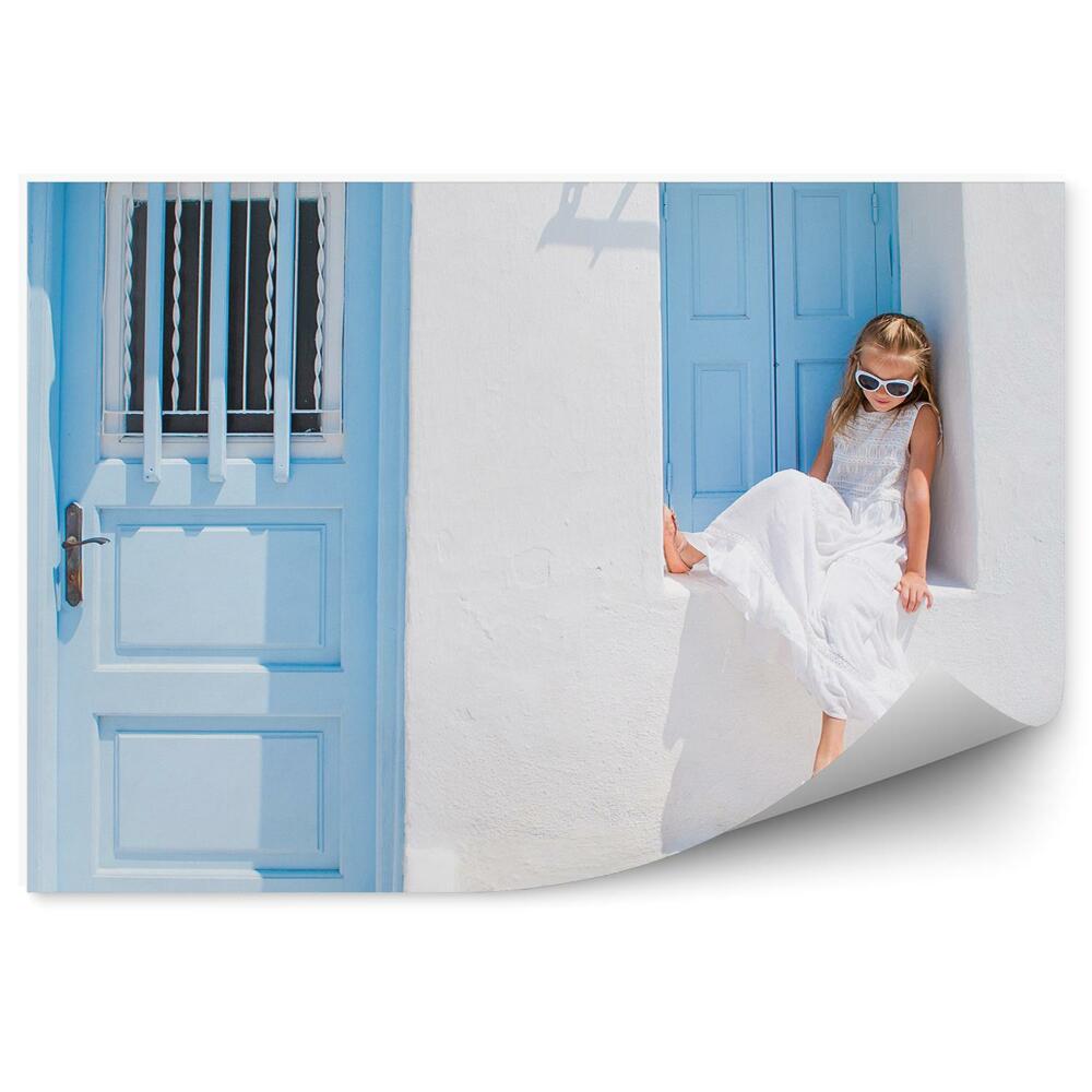 Fototapeta samoprzylepna Mała dziewczynka w niebieskim oknie biały budynek